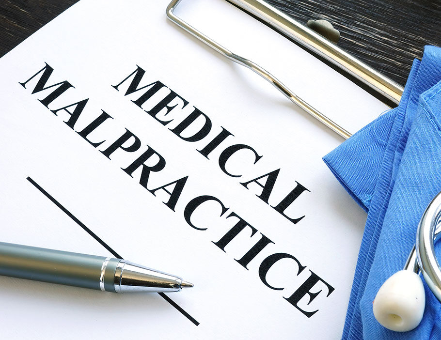 Medical malpractice printed on a sheet of paper on a clipboard, medical equipment visible.